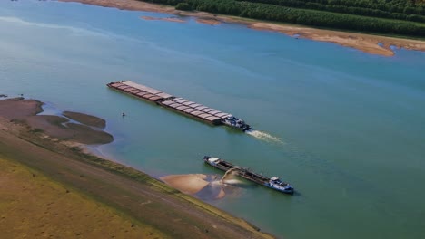 Aerial-shot-of-a-dredger-unloading-dredged-sand-on-a-big-river,-other-ships-passing-by,-sunny-day