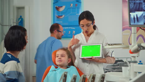 Dentista-Mostrando-Pantalla-Verde-A-La-Madre-Del-Pequeño-Paciente