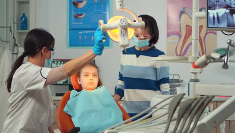 Médico-Dentista-Pediátrico-Que-Trabaja-En-La-Unidad-Dental-Con-Una-Enfermera-Y-Una-Niña-Paciente