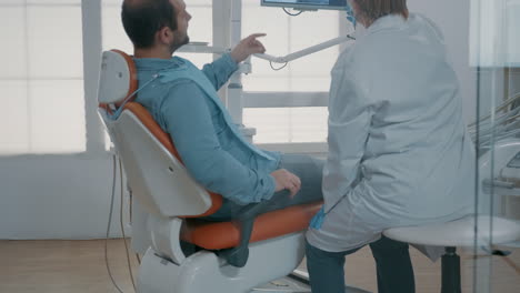 Mature-dentist-pointing-at-teeth-radiography-on-monitor