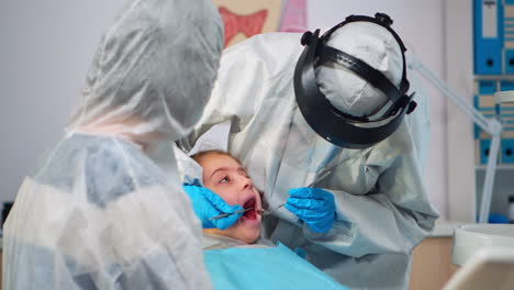 Close-up-of-dentist-in-coverall-examining-girl-patient-in-new-normal-dental-unit
