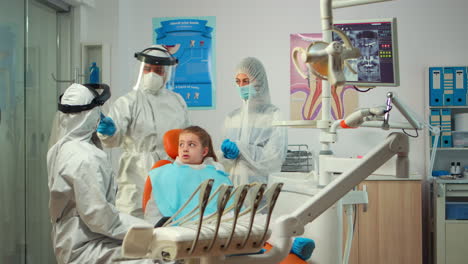 Dentista-Pediátrico-Usando-Traje-De-Protección-Tratando-A-Una-Paciente-Niña