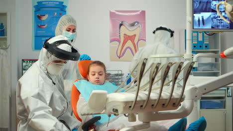 Dentista-Pediátrico-Con-Traje-Protector-Encendiendo-La-Lámpara-Hasta-El-Examen