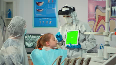 Dentist-with-face-shield-pointing-at-green-screen-display-talking-to-child