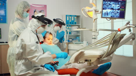 Técnico-Dental-En-Equipo-De-Protección-Encendiendo-La-Lámpara-Para-Examinar-Al-Niño