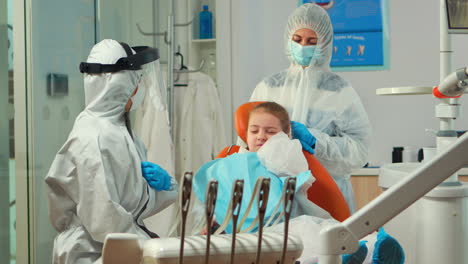 Child-in-protection-suit-showing-dental-problem-to-orthodontist