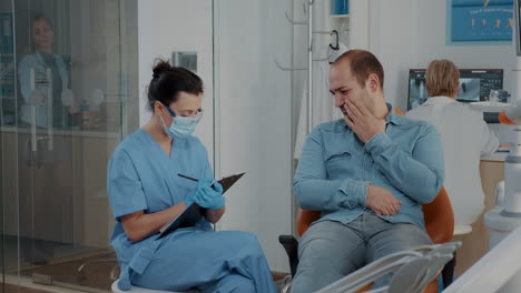 Enfermera-De-Odontología-Tomando-Notas-Y-Hablando-Con-El-Paciente-Sobre-El-Dolor-De-Muelas