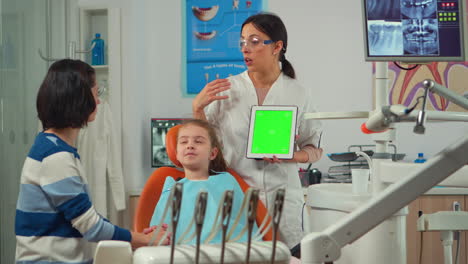 Pediatric-dentist-standing-near-girl-patient-pointing-at-green-screen-display