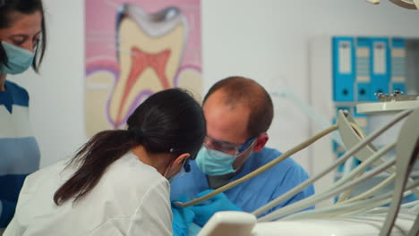 Close-up-view-of-pediatric-dentist-and-assistant-cleaning-tooth-for-little-girl