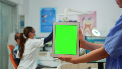 Close-up-of-tablet-with-green-screen-display-held-by-dental-assistant