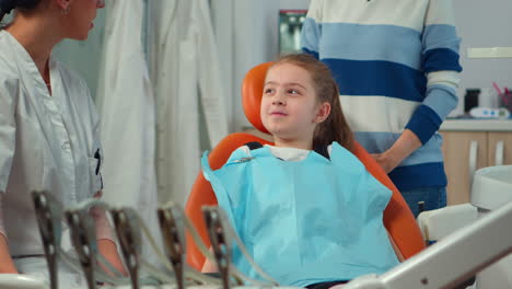 Close-up-of-kid-patient-with-toothache-wearing-dental-bib-talking-with-dentist