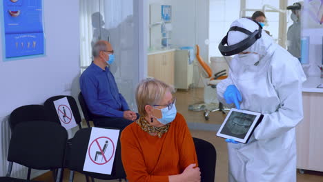 Dentist-doctor-with-face-shield-pointing-on-tablet-display