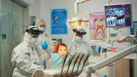 Dentistry-doctor-in-protective-suit-using-sterilized-dental-tools-examining-kid-patient
