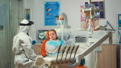Stomatologist-in-ppe-suit-holding-plaster-model-of-the-mandible-speaking-with-girl