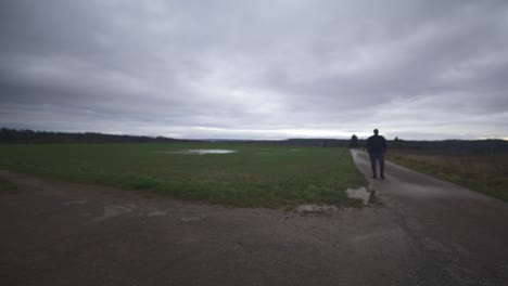 Modern-Black-Male-Waiting-in-Open-Field-Under-Grey-Sky,-Europe,-4K-|-Muscular,-Intimidating,-Shadow,-Figure,-Blurry,-Dark-Clothes,-Powerful,-Blurry,-Distant-Walk,-Puddle,-Thought,-Thinking,-Searching