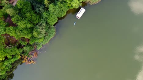 Top-down-shot-of-several-boats-floating-on-a-lake-next-to-a-very-colorful-forest-with-a-small-road-leading-through-it-in-Brandenburg,-Germany
