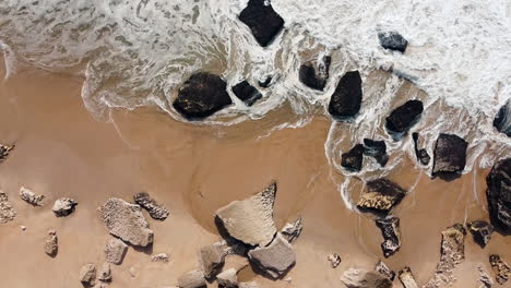 Aerial-top-down-shot-of-splashing-water-of-sandy-beach-during-sunny-day