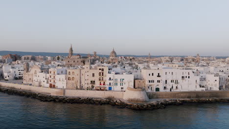 Static-aerial-footage-of-the-coastal-town-of-Monopoli,-Italy-with-the-calm-waves-of-the-Mediterranean-Sea-washing-up-against-the-wall-of-the-town