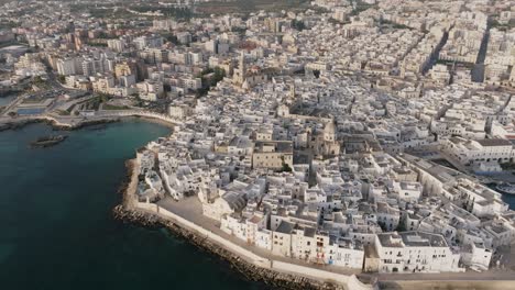 Wide-aerial-rotating-footage-of-the-town-of-Monopoli,-Italy-in-the-light-of-the-sunrise-and-the-blue-water-of-the-Mediterranean