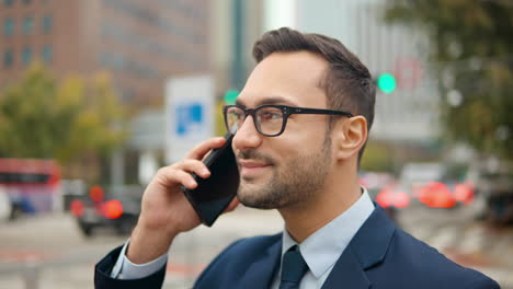 Portrait-of-a-Happy-Businessman-Talking-on-Mobile-Phone-Standing-at-Busy-City-Street-with-Traffic-Blurred-in-Background