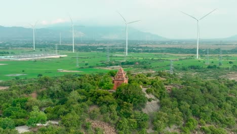 Drone-view-of-Porome-tower-,-ancient-tower-of-Champa-in-Ninh-Thuan-province,-far-away-is-a-wind-turbine-farm-combine-with-solar-power-station,-central-Vietnam