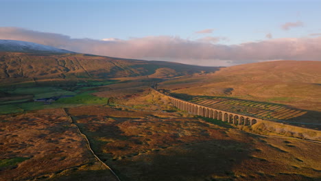 Establishing-Aerial-Drone-Shot-of-Ribblehead-Viaduct-with-Snowy-Whernside-Behind-at-Sunset-Golden-Hour-in-Yorkshire-Dales-UK