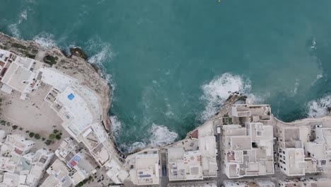 Top-down-aerial-footage-of-the-town-of-Polignano-a-Mare-and-the-seaside-cliffs-with-the-waves-of-the-Mediterranean-Sea-crashing-into-them