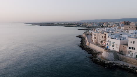 Aerial-footage-rotating-around-the-coastal-town-of-Monopoli,-Italy-showing-off-the-buildings-that-are-right-on-the-waters-of-the-Mediterranean