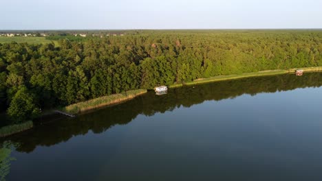 Small-houseboat-floating-in-a-lake-next-to-a-forest-in-Brandenburg,-Germany