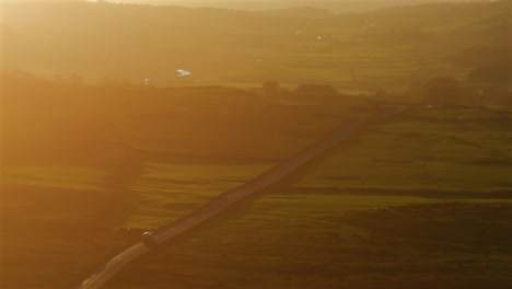Lange-Objektiv-Drohnenaufnahme-Eines-Lastwagens,-Der-Bei-Sonnenuntergang-Durch-Den-Dunst-Die-Straße-In-Den-Yorkshire-Dales-Entlangfährt
