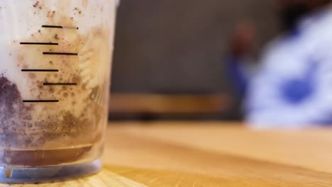 an-ice-coffee-in-the-foreground-of-the-frame-while-a-heavy-set-African-American-black-male-in-the-blurred-background-is-having-a-conversation