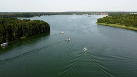 Three-motor-boats-driving-on-a-lake-next-to-a-forest-in-Brandenburg,-Germany