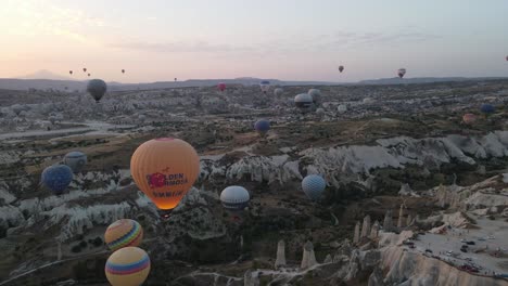 Drone-view-of-dozens-of-tourist-balloons-flying-in-the-valley-near-sunrise,-Turkey-Cappadocia