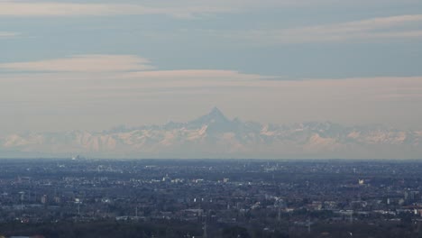 Mount-Monviso-in-far-distance-and-Lombardia-town-bellow,-static-aerial-view