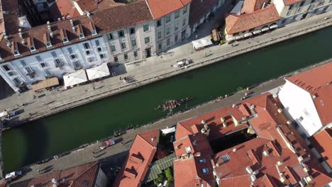 People-row-in-Navigli-canal-surrounded-with-majestic-architecture,-aerial-view