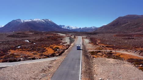 Siguiendo-A-Un-Vehículo-Circulando-Por-Una-Carretera-Vacía-Con-Montañas-Nevadas-Al-Fondo