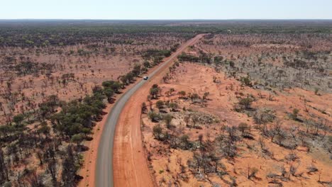 Aerial-view-of-a-country-sealed-road-while-a-a-car-towing-a-caravan-passing-by-in-the-Australian-outback