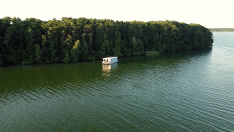 Small-house-boat-floating-on-a-lake-next-to-a-forest-and-several-other-motor-boats-in-Brandenburg,-Germany