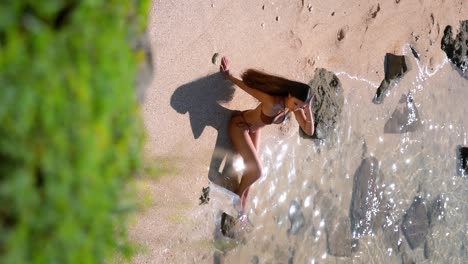 The-bikini-clad-model's-magnetic-beauty-is-vividly-captured-in-a-vertical-video,-highlighting-her-graceful-movements-and-alluring-presence-as-she-graces-the-sandy-shore