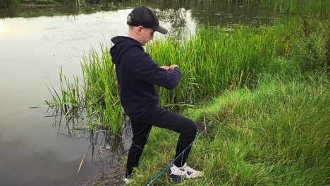 A-young-boy-by-the-side-of-a-fishing-lake-puts-bait-on-the-fishing-line-hook