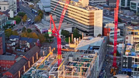 Construction-site,-red-cranes-and-street-traffic-in-Sheffield,-aerial