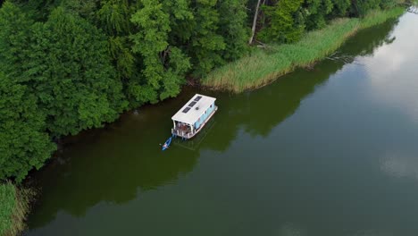 Kleines-Hausboot,-Das-Auf-Einem-Von-Einem-Wald-Umgebenen-See-In-Brandenburg,-Deutschland,-Schwimmt
