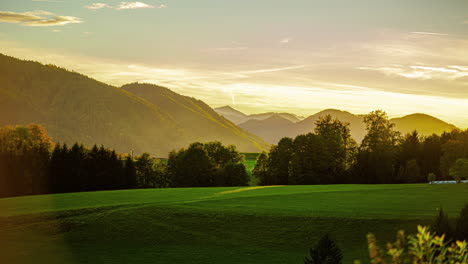 Ein-Sonnenaufgang-Mit-Gelbem-Schein-über-Einer-Grünen-Landschaft-Mit-Bergen-Und-Wiesen