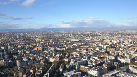 Vast-city-of-Milan-with-mountain-range-of-Alps-in-far-distance,-aerial-view