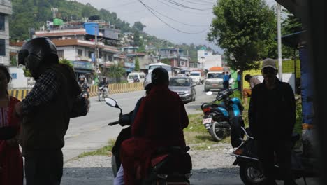 Rear-view-of-Nepalese-motorbike-taxi-drivers-waiting-in-the-shade-of-building,-silhouettes-against-village-background