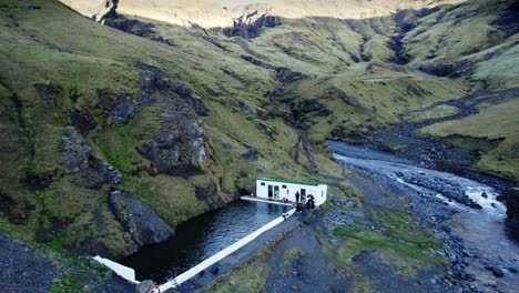Remote-thermal-bath-in-rural-Iceland,-vast-volcanic-mountain-landscape,-drone