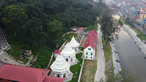 Drone-pullback-reveals-Nepalese-temples-at-base-of-mountain-along-riverside