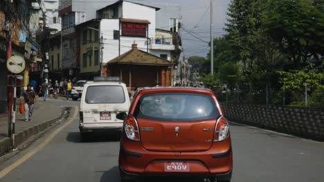 Red-and-white-compact-cars-drive-in-Nepalese-town-on-road-at-midday,-slow-motion