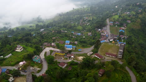 Bird's-eye-view-of-vibrant-colorful-village-in-hill-town-of-Nepal-as-clouds-settle-in-valley-below