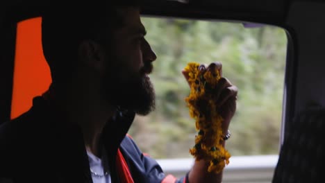 Man-with-full-beard-holding-yellow-prayer-flowers-stairs-dramatically-out-window-of-car